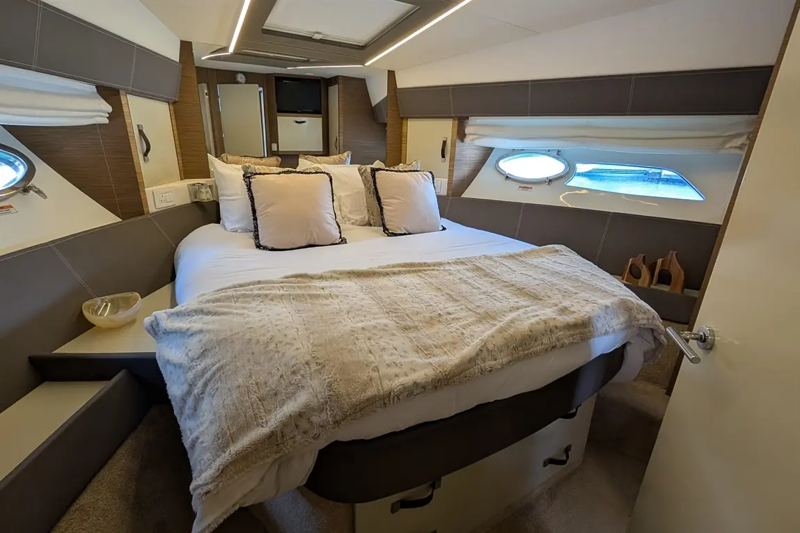 Luxury boat bedroom featuring a double bed with decorative cushions, soft blanket, and porthole windows offering light.
