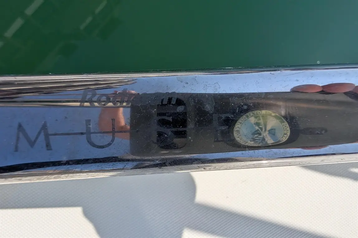 Reflection on a shiny surface showing “Rodini M-U E” text and a round badge featuring a mountain and water scene.