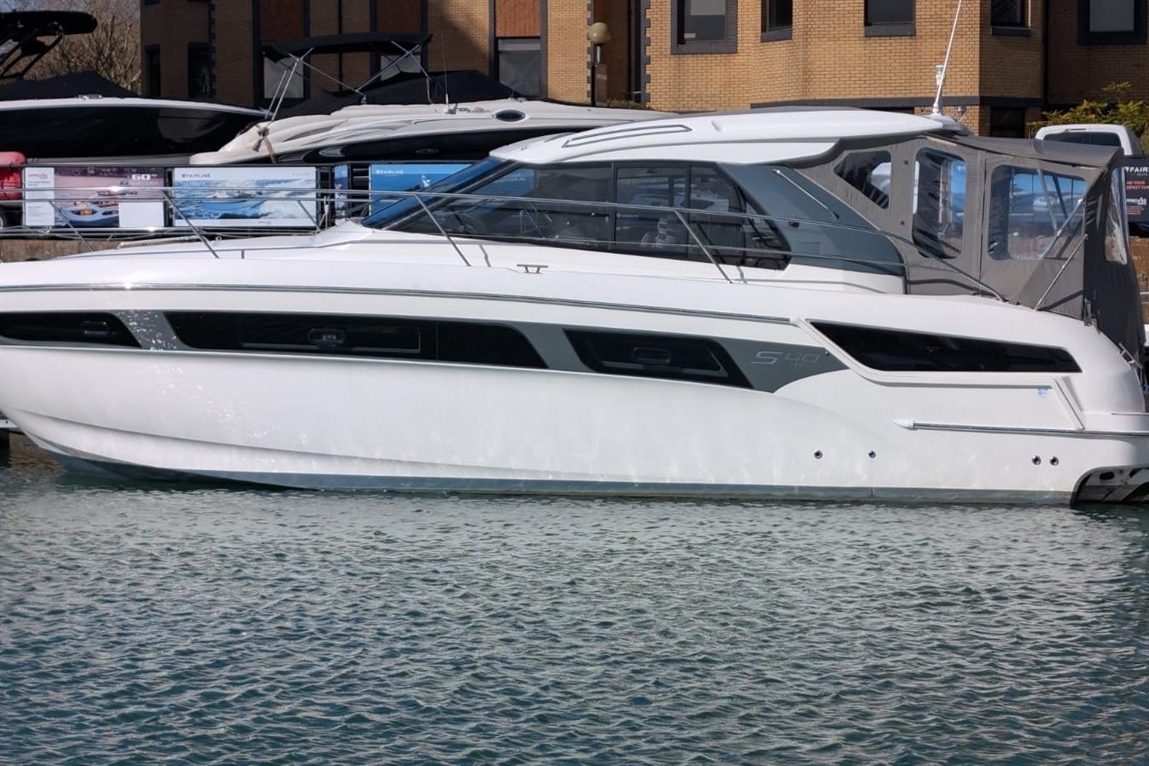 A sleek white boat, model S40, docked in calm water with buildings and other boats in the background.