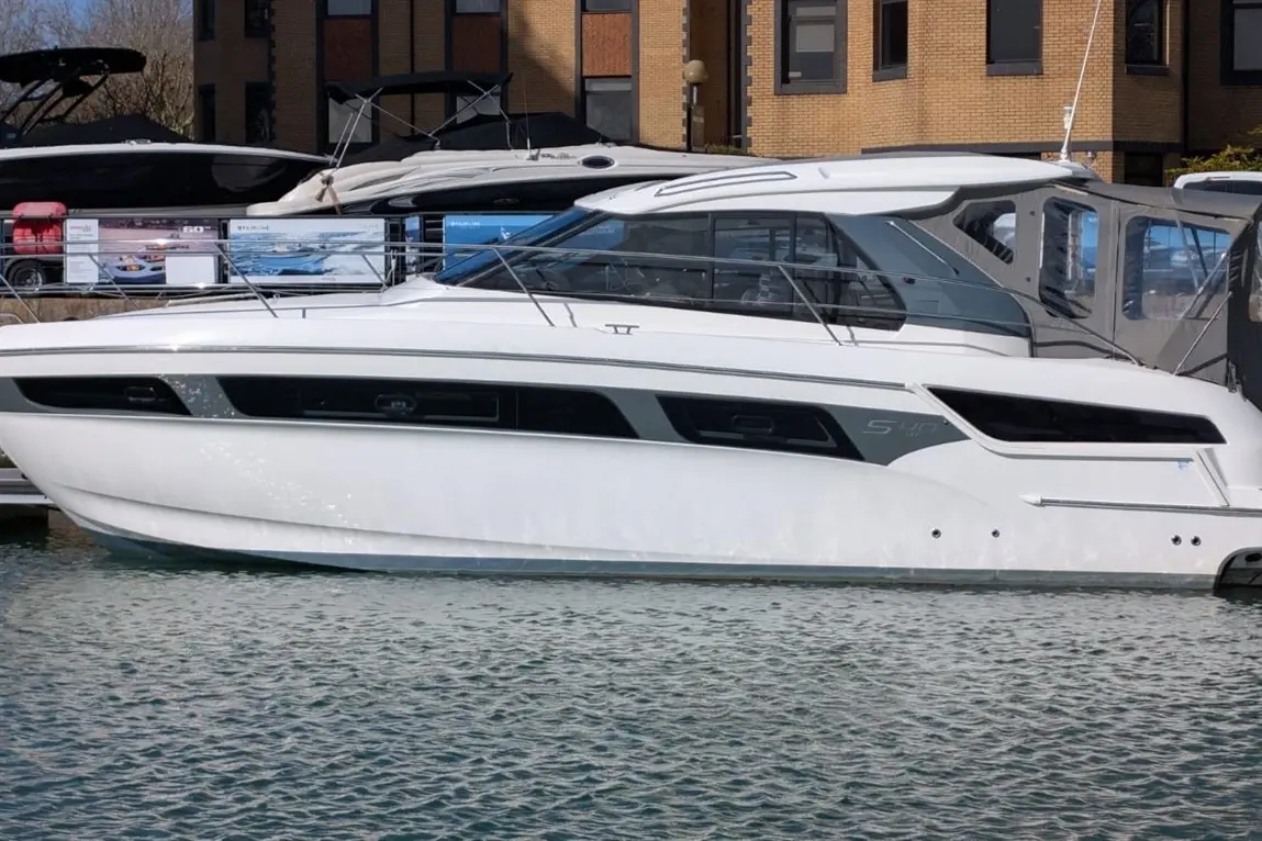 A white luxury motorboat is docked in the water, featuring sleek design and large windows, with other boats in the background.