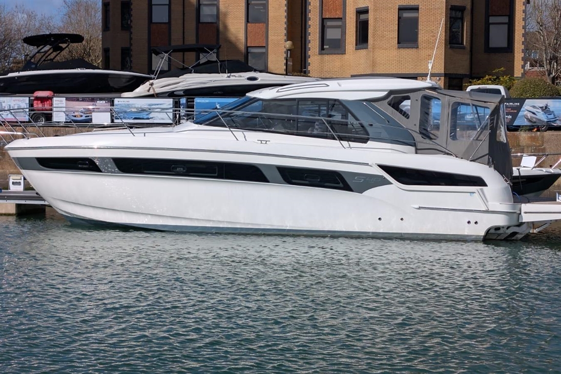 Sleek white motor yacht docked in calm waters, showcasing large windows and modern design features against a sunny backdrop.