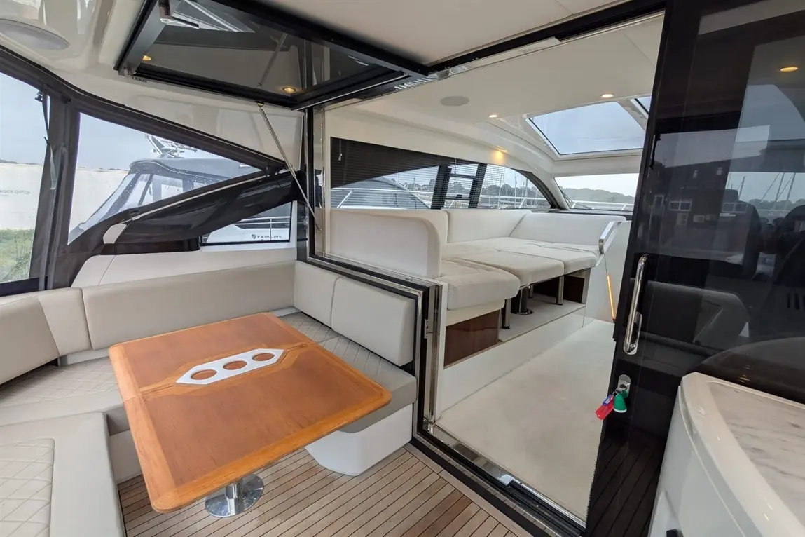 Interior of a modern boat featuring a wooden table, plush seating, and large windows, with a view of the marina outside.