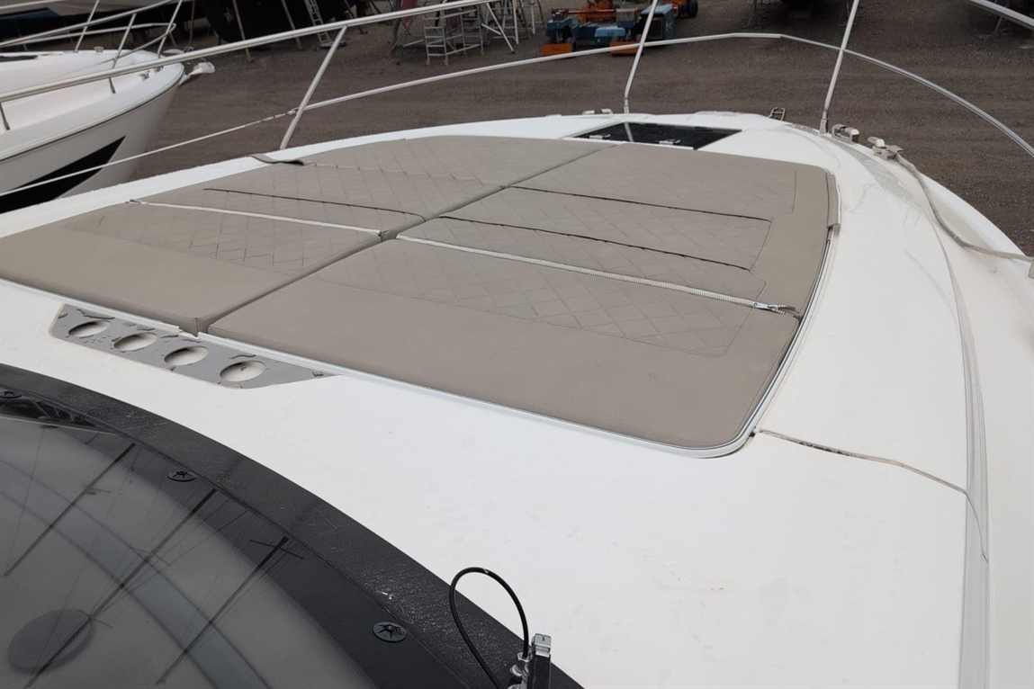 Top view of a boat with beige cushioned pads on the deck and a black-tinted windshield edge visible.