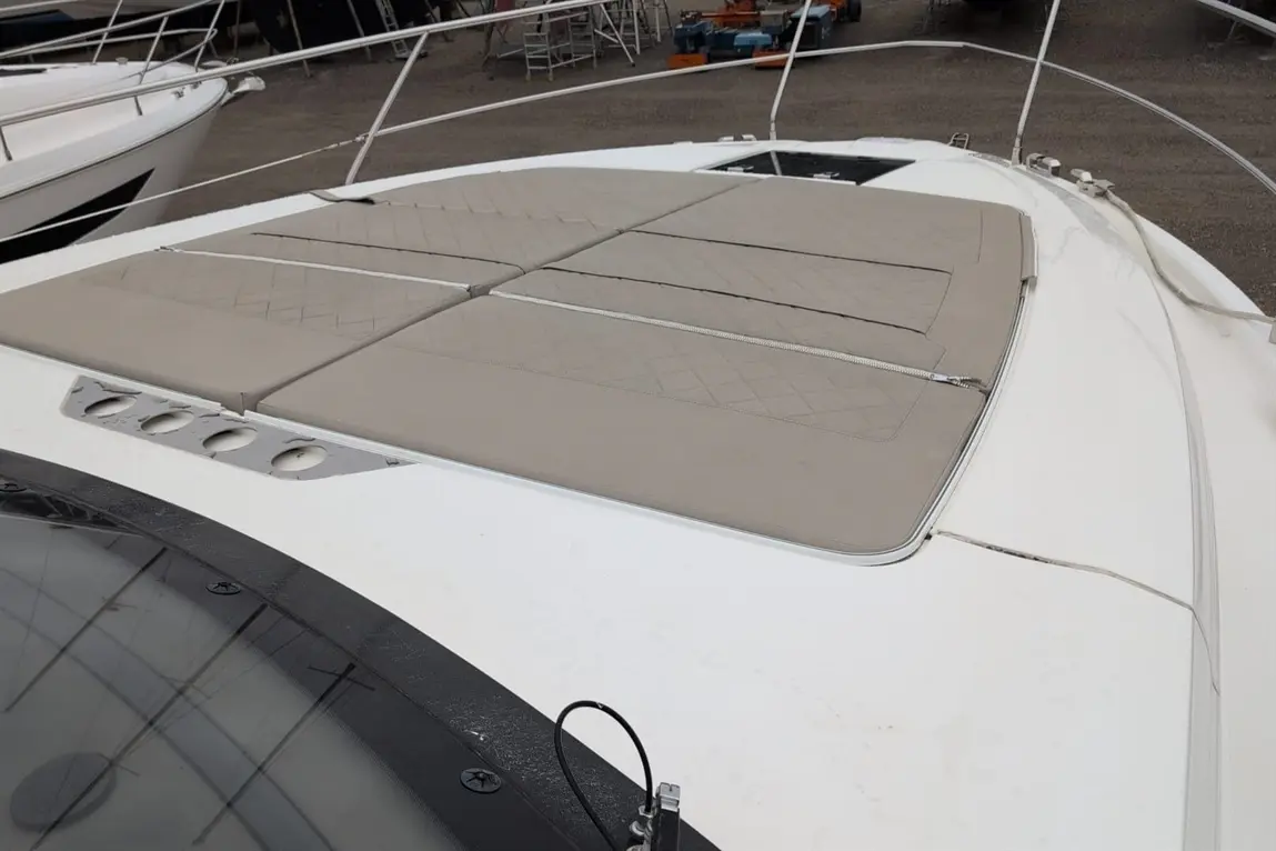 Top view of a boat with beige cushioned pads on the deck and a black-tinted windshield edge visible.