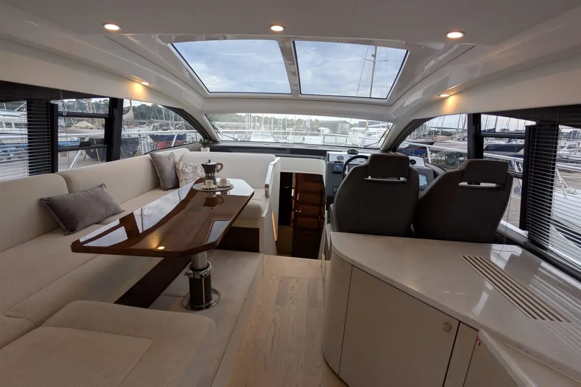 Interior of a modern yacht featuring a stylish seating area, wooden table, and navigation console with boats visible outside.