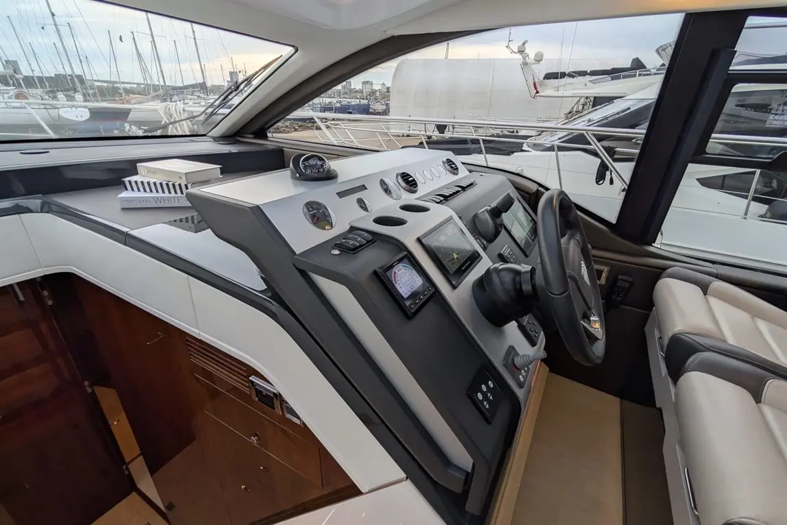 Luxury yacht cockpit featuring a steering wheel, control panels, and navigational screens, with boats visible in the background.