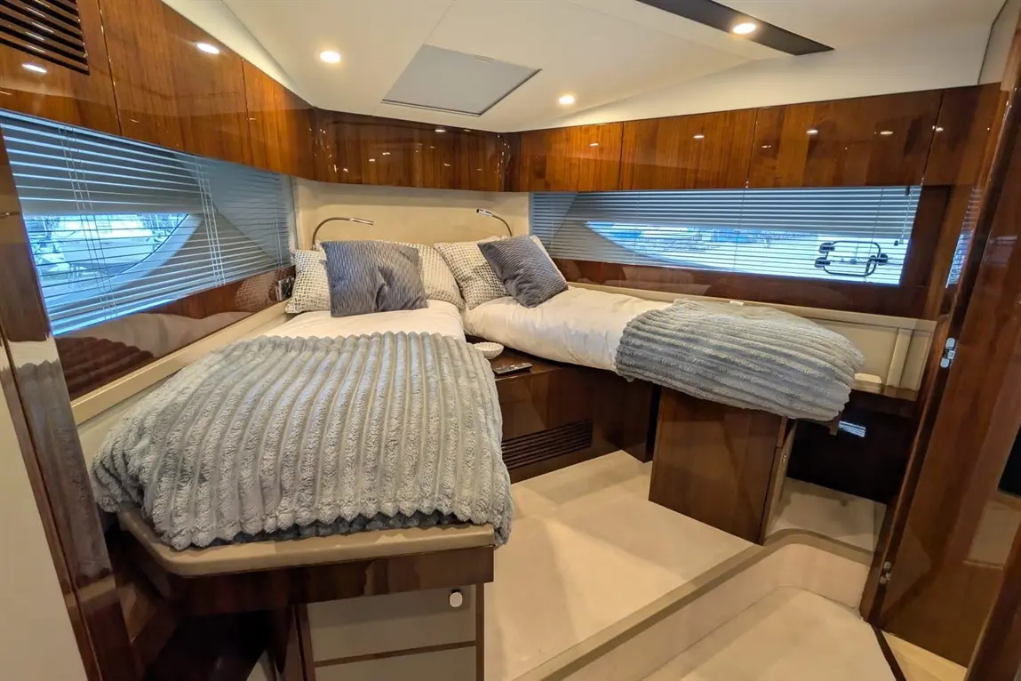 Luxurious boat cabin featuring two single beds with grey blankets and decorative pillows, wooden cabinetry, and a window view.