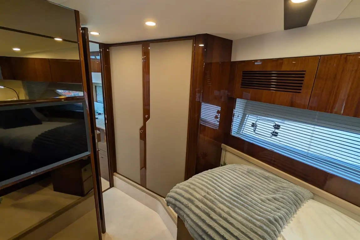 Interior of a modern yacht cabin featuring a bed, television, sliding door, and large windows with blinds.