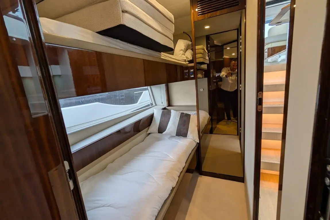 Modern boat cabin with twin bunks, mirrored wardrobe, plush bedding, and illuminated staircase leading to upper levels.