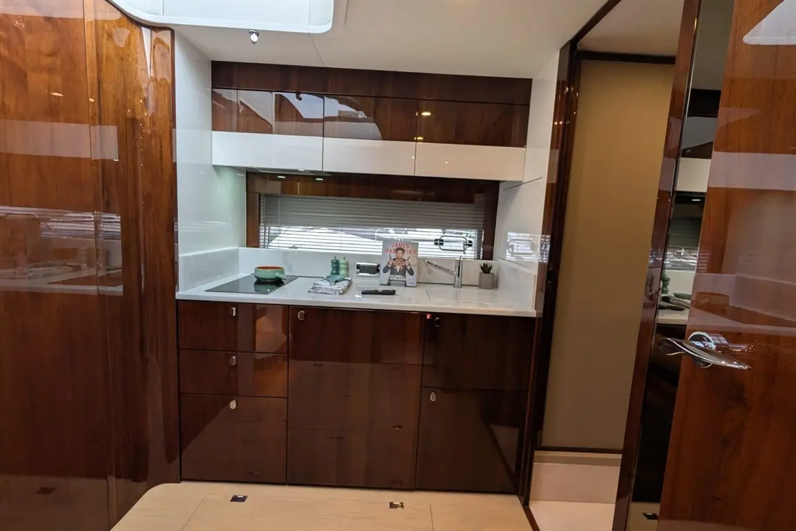 Modern yacht kitchen with sleek wooden cabinets, marble countertop, sink, and a cookbook displayed on the counter.
