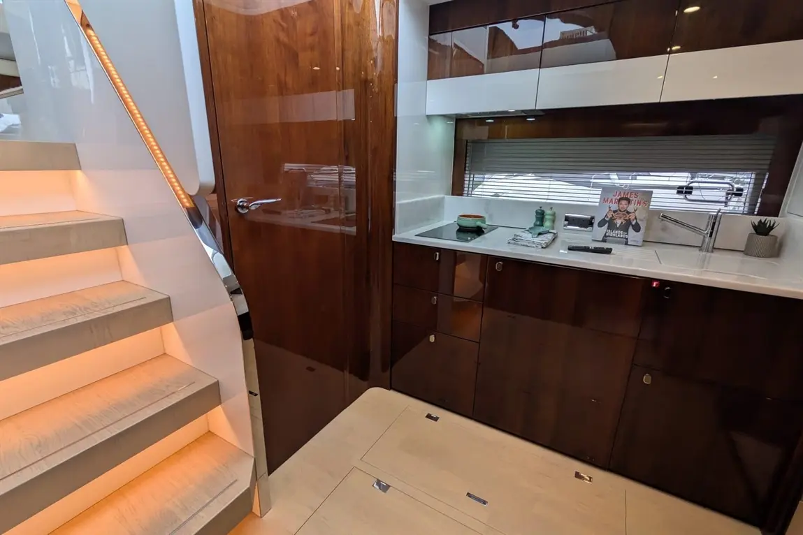 Modern yacht interior featuring a staircase, kitchen area with a magazine, and glossy wooden finishes.