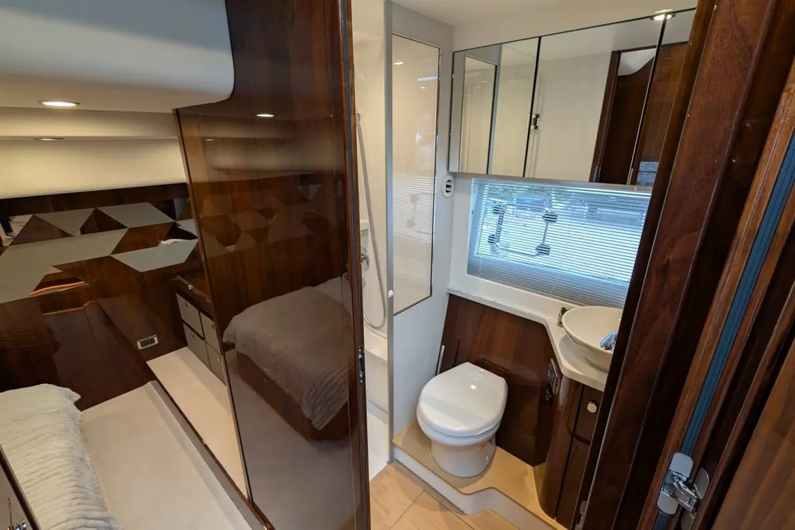 A modern, compact bathroom featuring a shower, toilet, sink, and wood-finished cabinetry, with natural light illuminating the space.