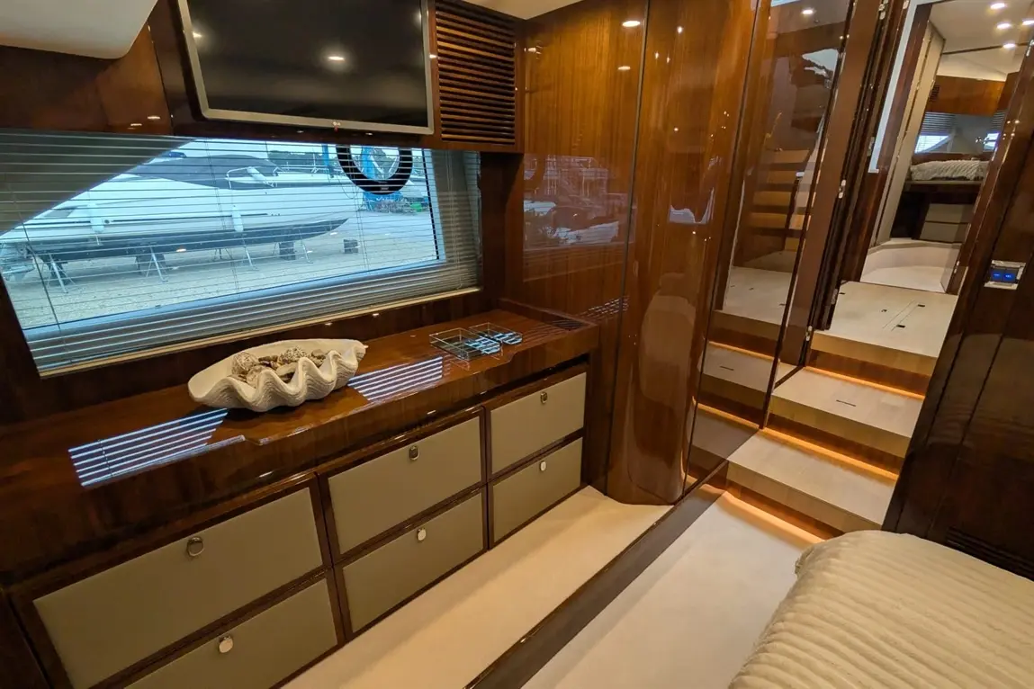 Luxurious yacht interior featuring polished wood drawers, a TV, and a view of a boat through a large window.