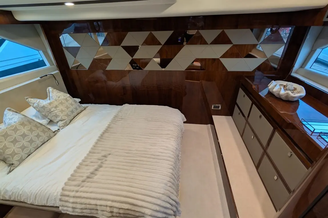 Luxurious boat bedroom featuring a plush bed, geometric wooden wall, decorative cushions, and a stylish dresser.