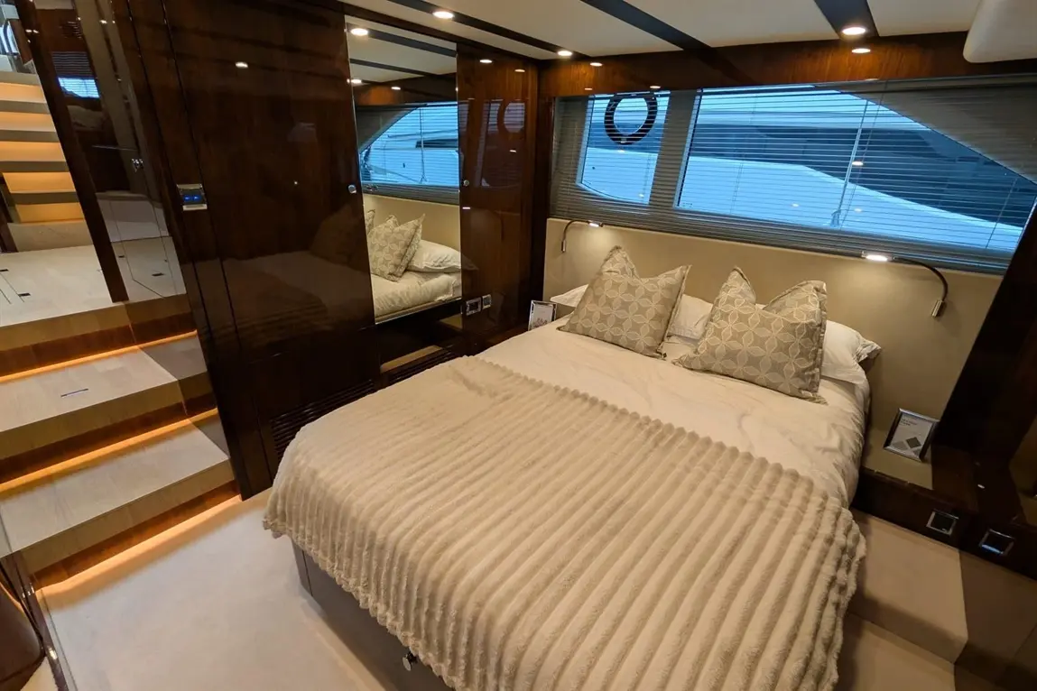 Luxury yacht bedroom featuring a double bed with a striped blanket, decorative pillows, and illuminated staircase in the background.