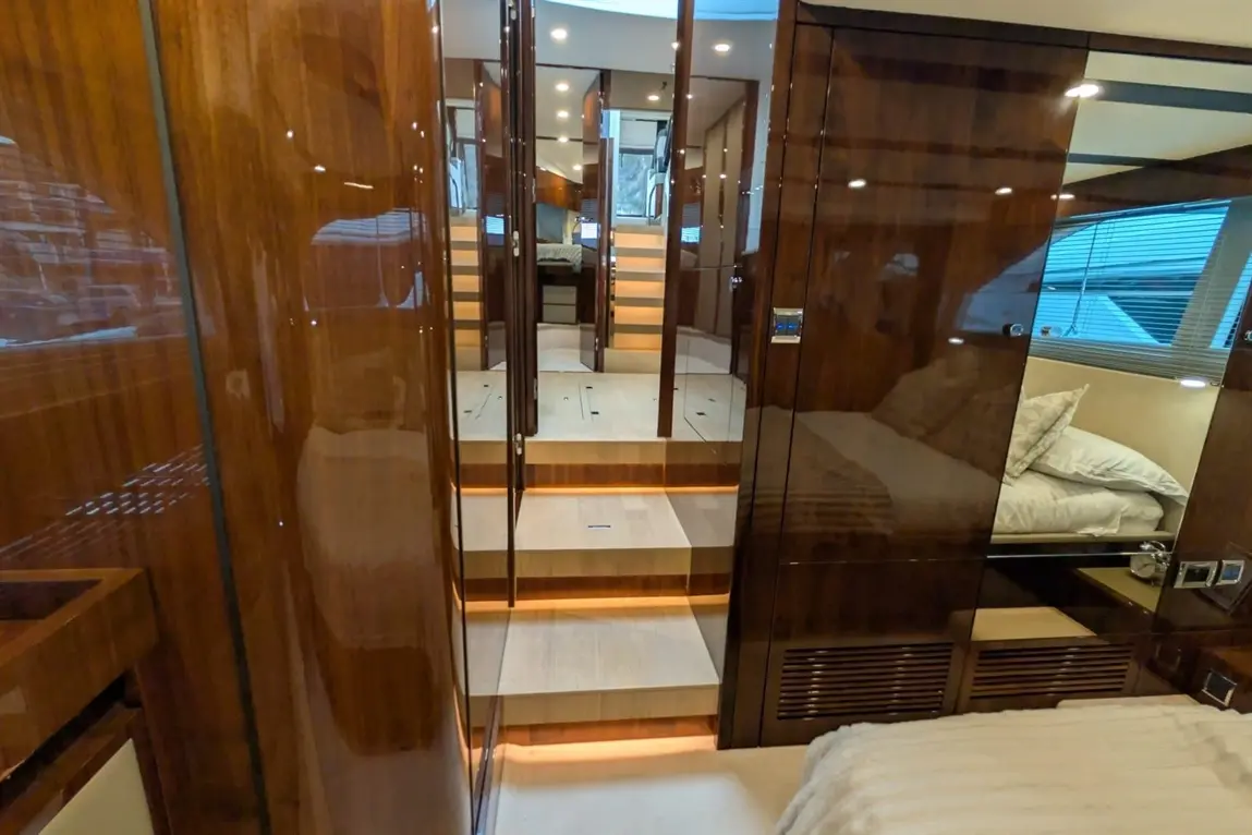 Interior of a luxury yacht showing polished wooden panels, stairs with soft lighting, and a well-furnished bedroom area.