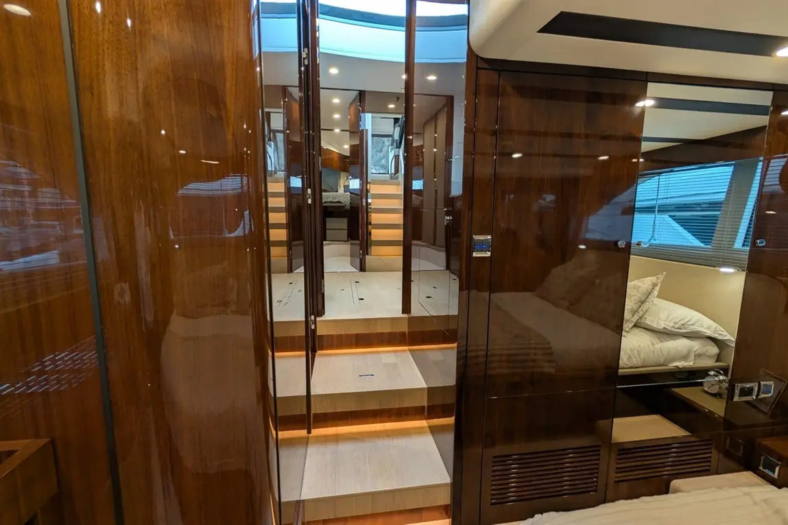 Modern yacht interior featuring polished wood, stairs leading to a cabin, and a bedding area with pillows and bedside lighting.