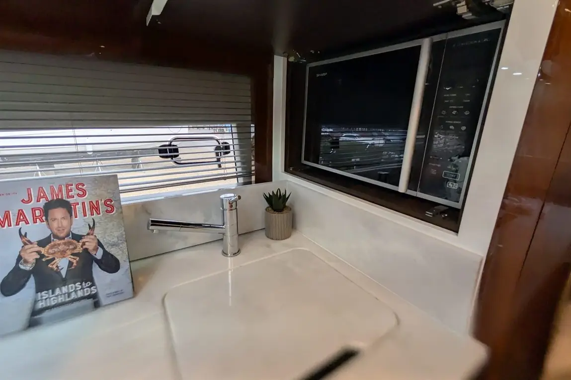 Modern kitchen area featuring a sink, James Martin's cookbook, and a microwave, with a potted plant in the background.