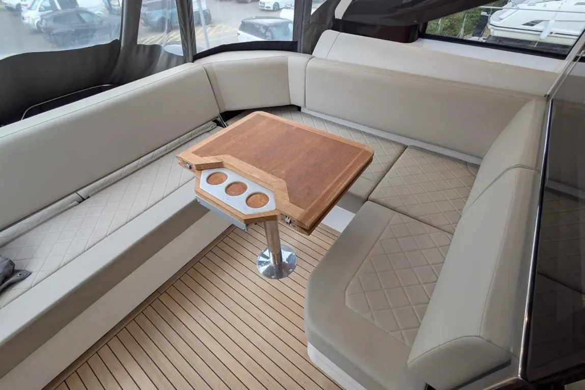 Luxurious boat interior featuring a cream leather seating area, a wooden table with cup holders, and a sleek wood floor.