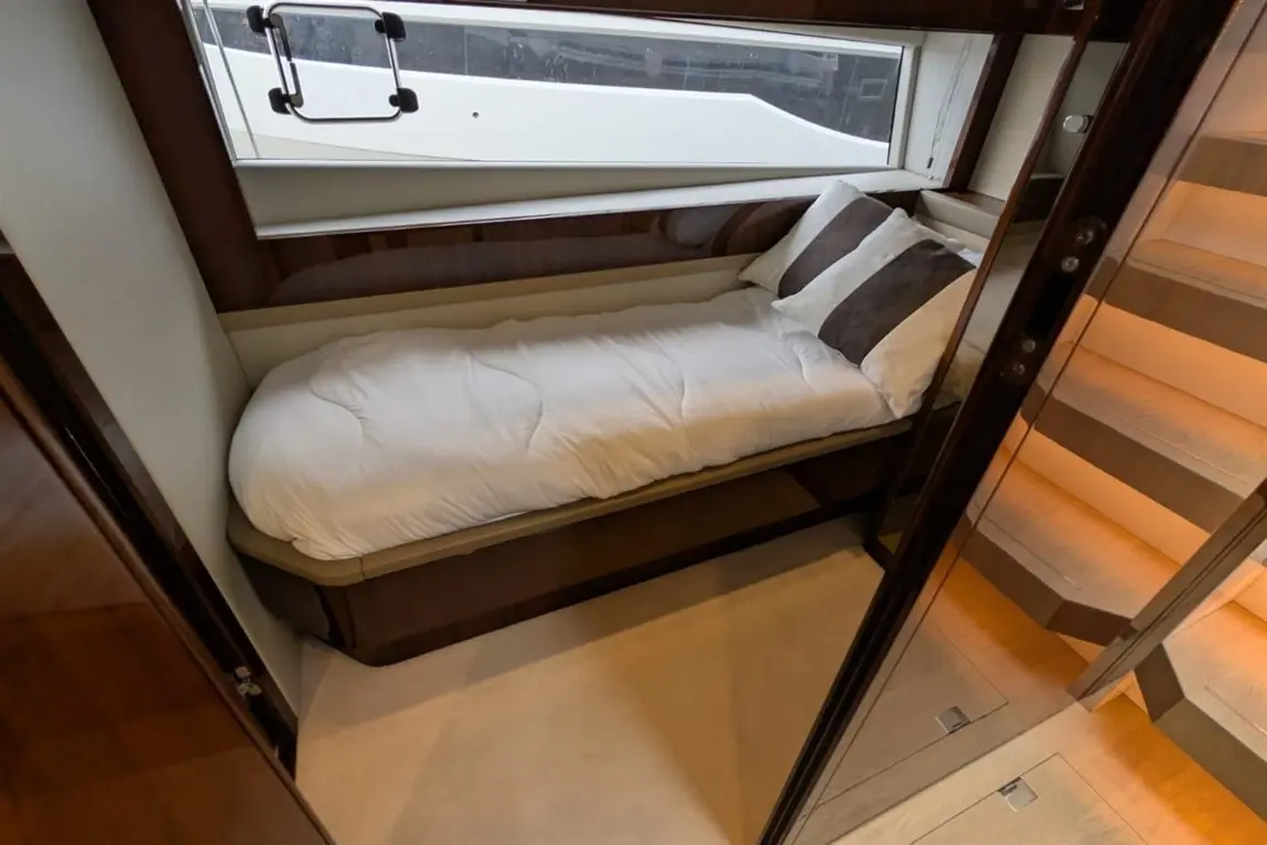Compact cabin featuring a single bed with white bedding and brown cushions, natural light from a window, staircase visible.