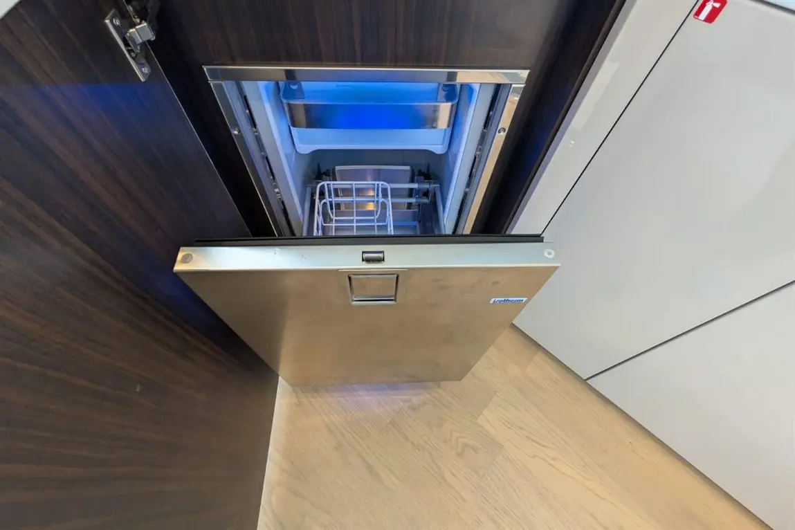 A partially open silver dishwasher reveals its interior, featuring a blue interior light and a white cutting tray.