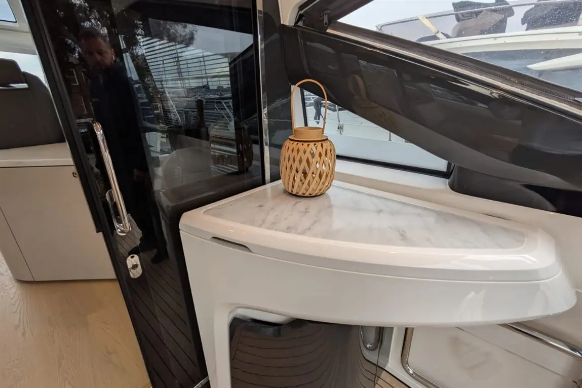 A modern yacht interior featuring a crescent marble top table with a woven lantern, reflecting natural light and outdoor views.