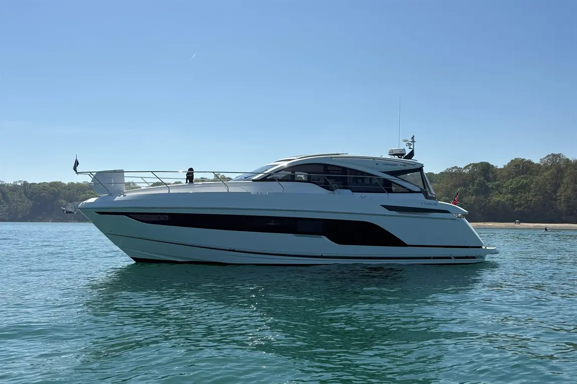Luxury motor yacht anchored in clear water, with a person standing on the deck, surrounded by a lush green shoreline.