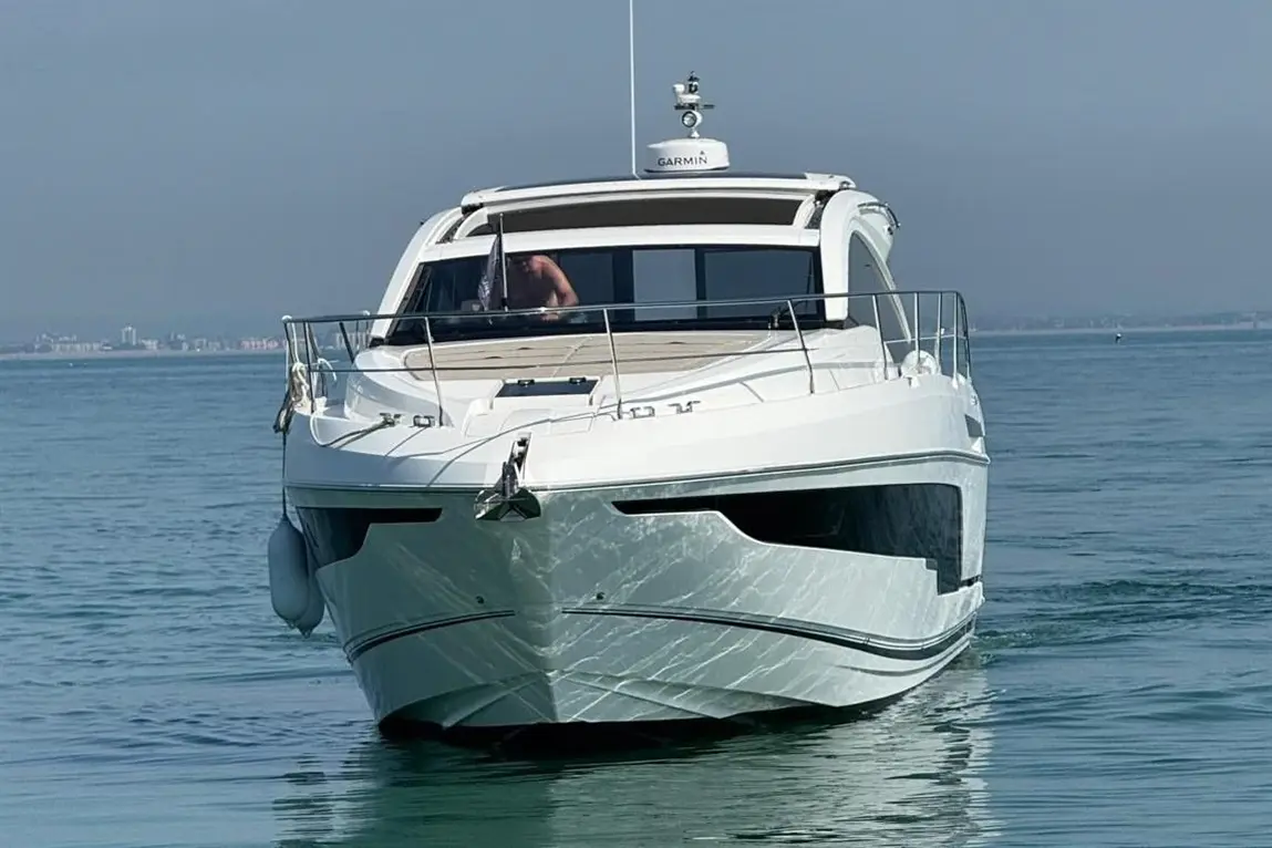 A sleek white motorboat navigates calm waters, with a person visible at the helm, and city skyline in the background.