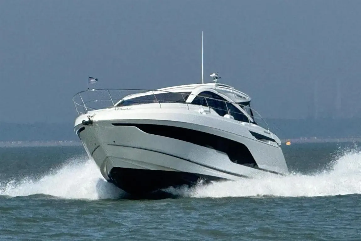 A sleek white yacht speeding across the water, creating waves, with a clear blue sky in the background.