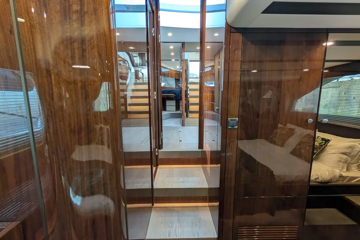 Luxurious yacht interior showing mirrored wooden panels, glass doors, and stairs leading to a cabin with a double bed.