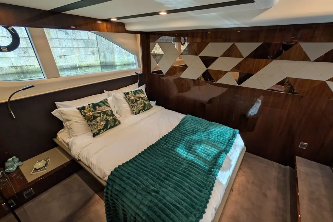 Modern bedroom featuring a double bed with tropical cushions, a teal throw, and geometric wall decor. Natural light from windows.