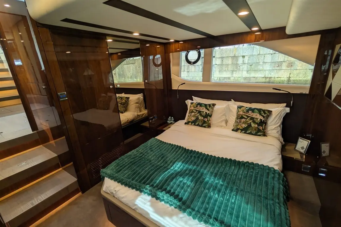 Luxurious boat bedroom featuring a double bed with green blanket, decorative cushions, and wooden finishes; stairs visible.