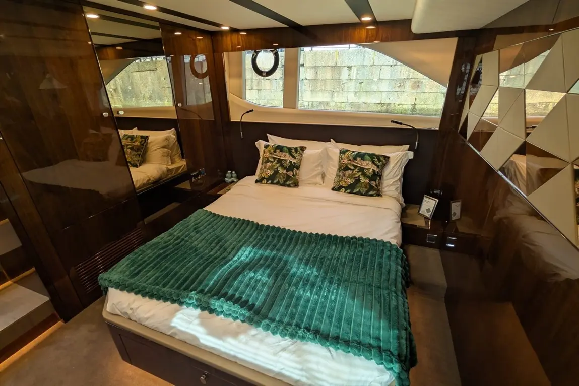Luxury boat cabin featuring a double bed with green throw, tropical cushions, mirrored walls, and soft ambient lighting.