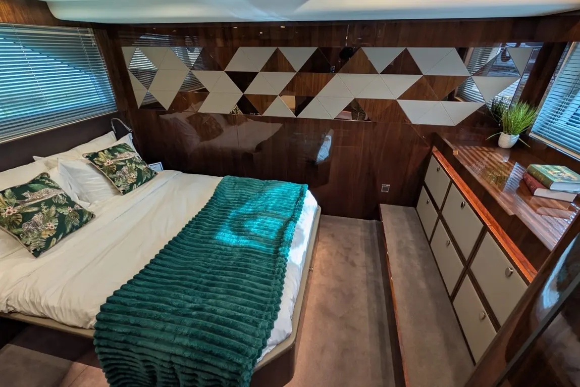 Stylish bedroom featuring a double bed with floral cushions, a teal throw, wooden decor, and a minimalist storage unit.