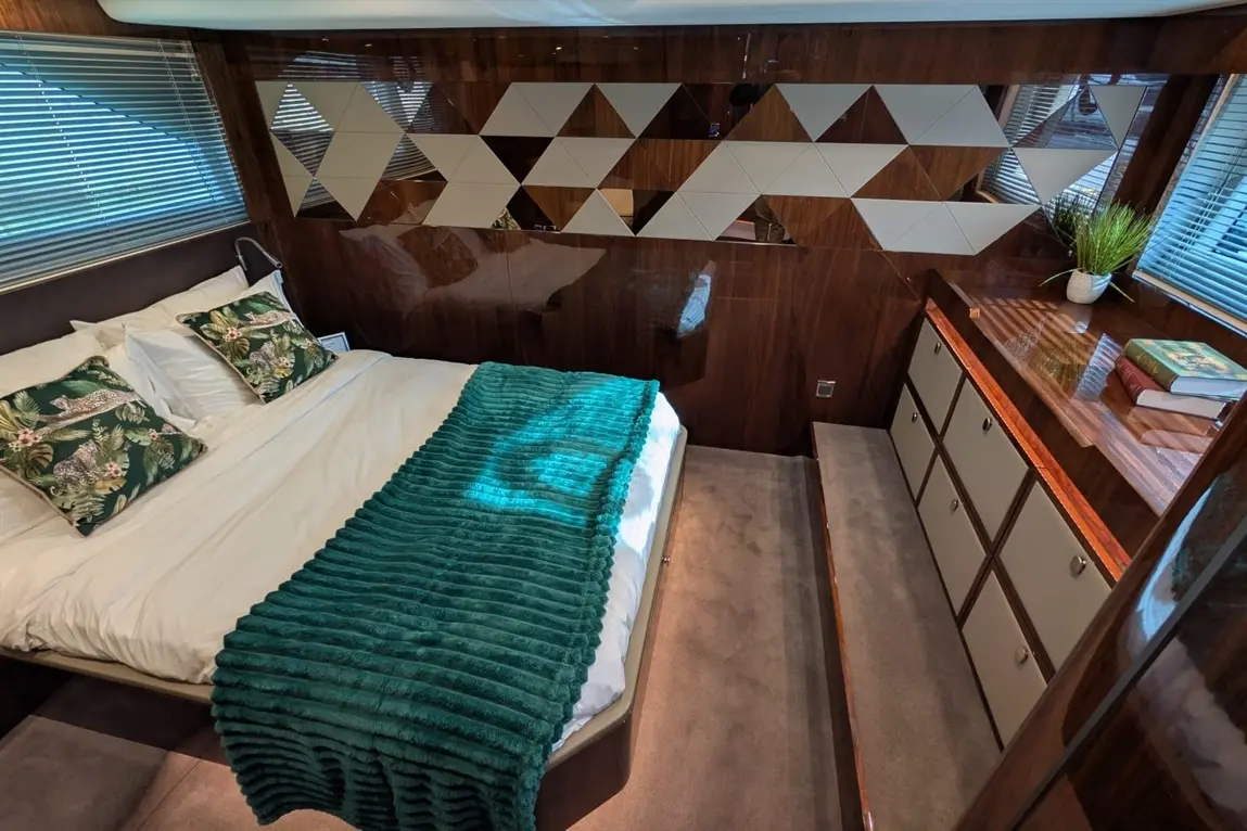 Modern bedroom featuring a double bed with tropical cushions, green throw, wooden storage, and geometric wall decor.