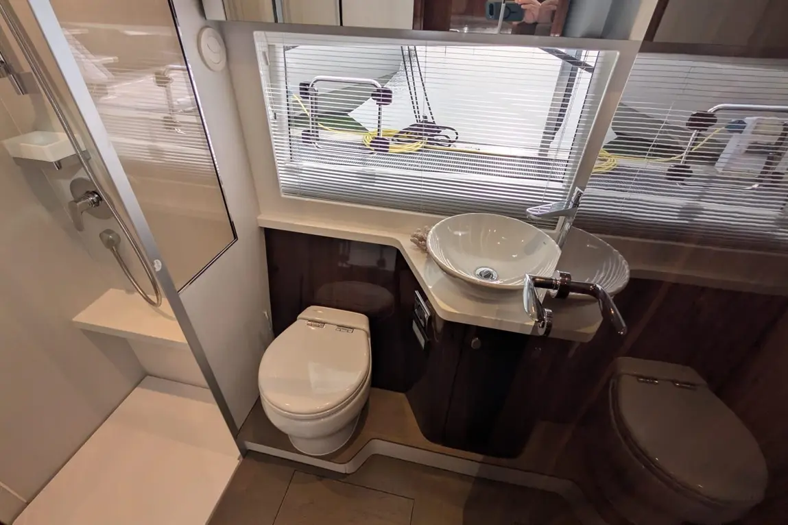 Modern bathroom featuring a shower, toilet, and a stylish washbasin near a window with blinds.