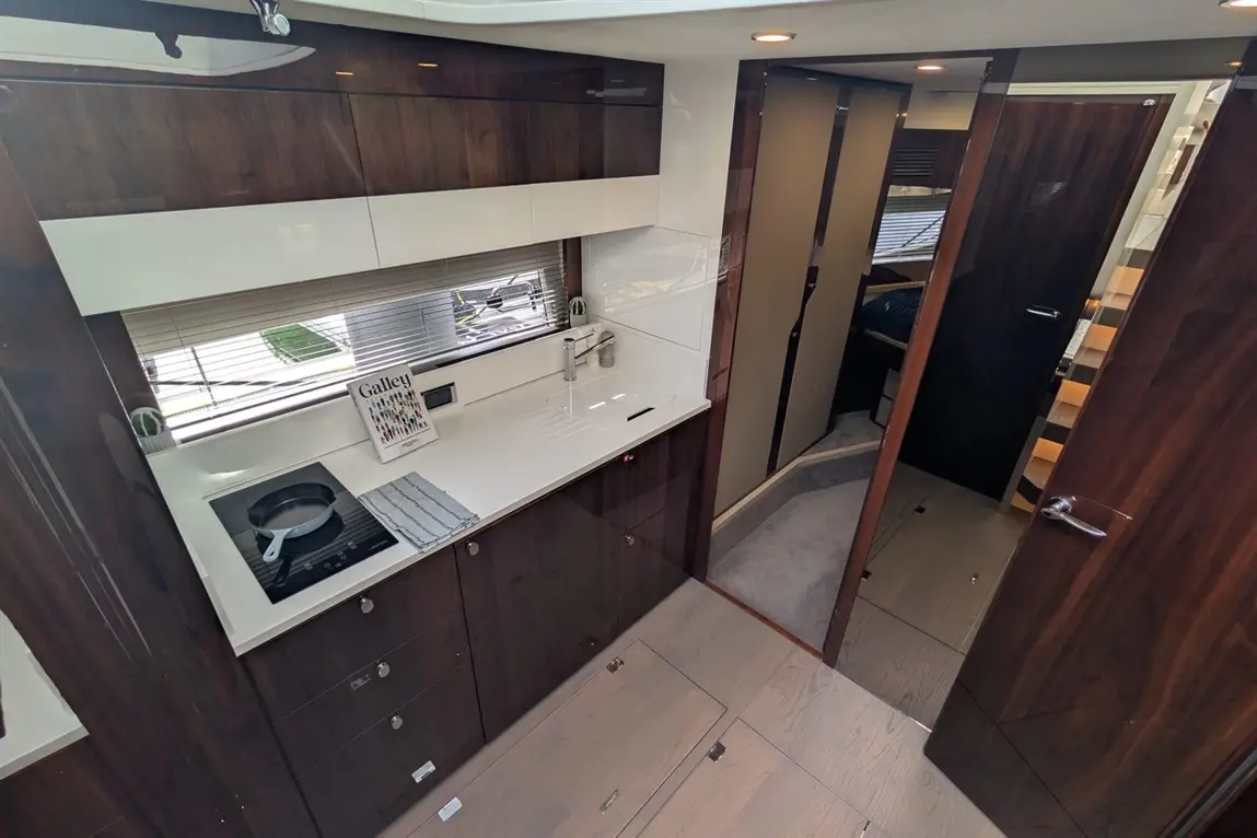 Modern yacht galley with dark wood cabinetry, an induction stove, and a magazine titled "Galley" on the counter.