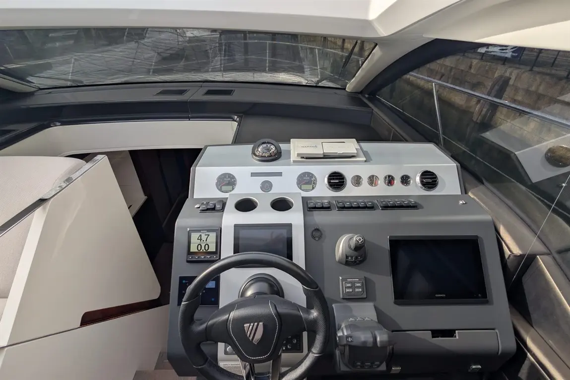 Luxury yacht cockpit with steering wheel, digital displays, gauges, and Garmin device; modern design and nautical instruments visible.