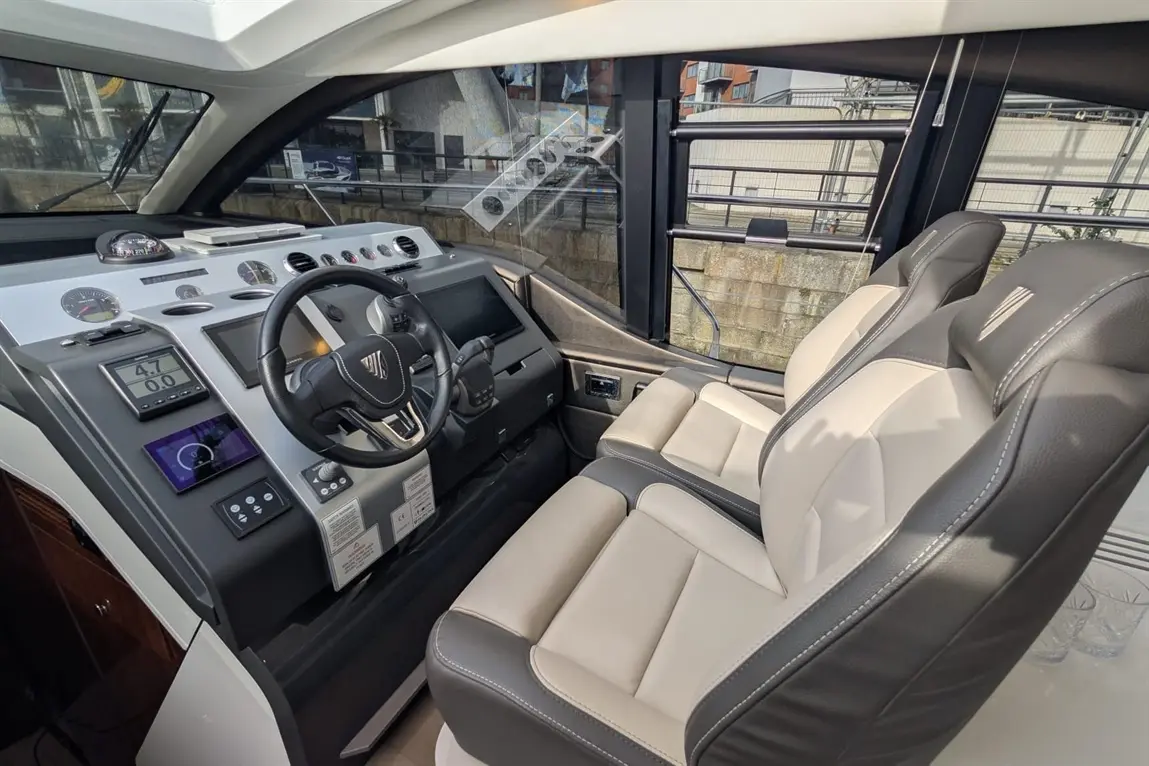 Luxury boat interior featuring a sleek dashboard, steering wheel, and two leather seats with a view through large windows.