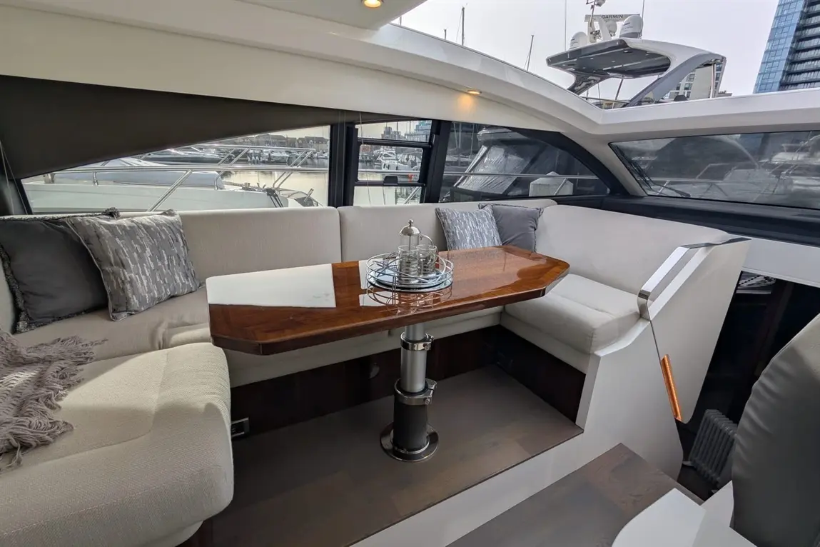 Interior of a boat featuring a soft seating area and a polished wooden table with glasses on a silver tray, overlooking the marina.