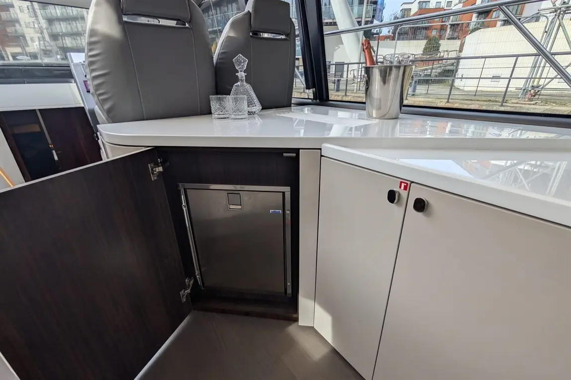 Modern boat interior featuring a compact fridge, glassware, and a champagne bucket on a sleek white table.
