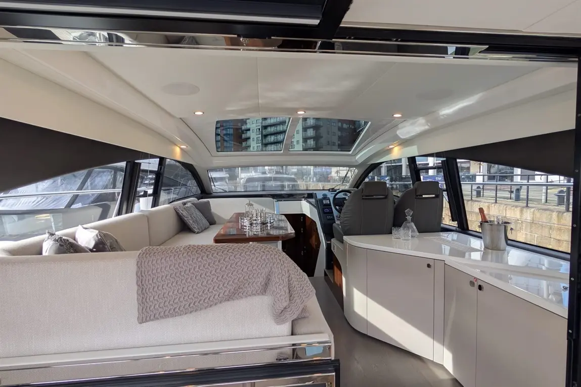 A luxurious yacht interior featuring a spacious lounge, dining table, and helm with panoramic windows and modern decor.