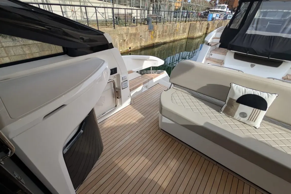 Luxury boat interior featuring a cushioned bench, wooden flooring, and a view of the docked marina. Decorative pillow visible.