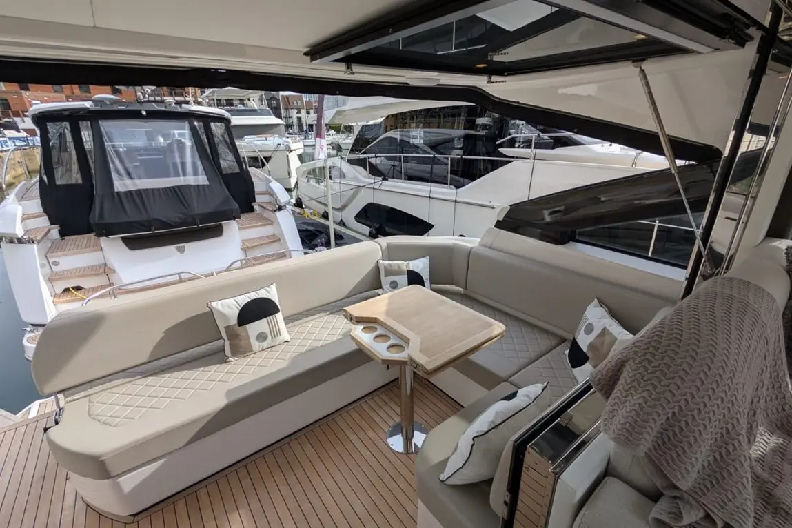 Luxury yacht interior with a stylish seating area, wooden table, and decorative cushions, overlooking the marina.