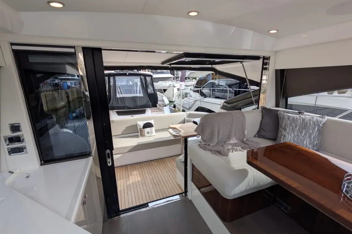 Interior view of a luxury boat, featuring plush seating, wooden table, and a bright entrance to the outdoor deck with other boats visible.
