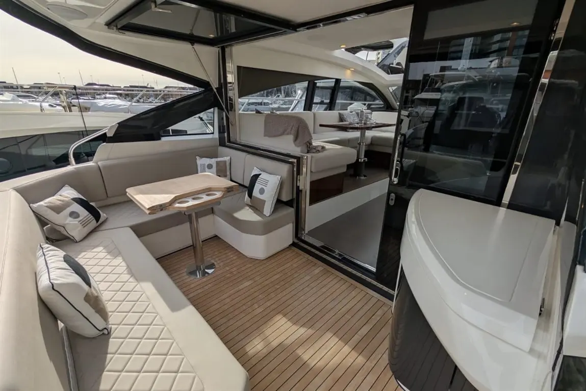 Luxury yacht interior featuring sleek seating, a wooden table, and marina views through large windows. Plush cushions enhance comfort.