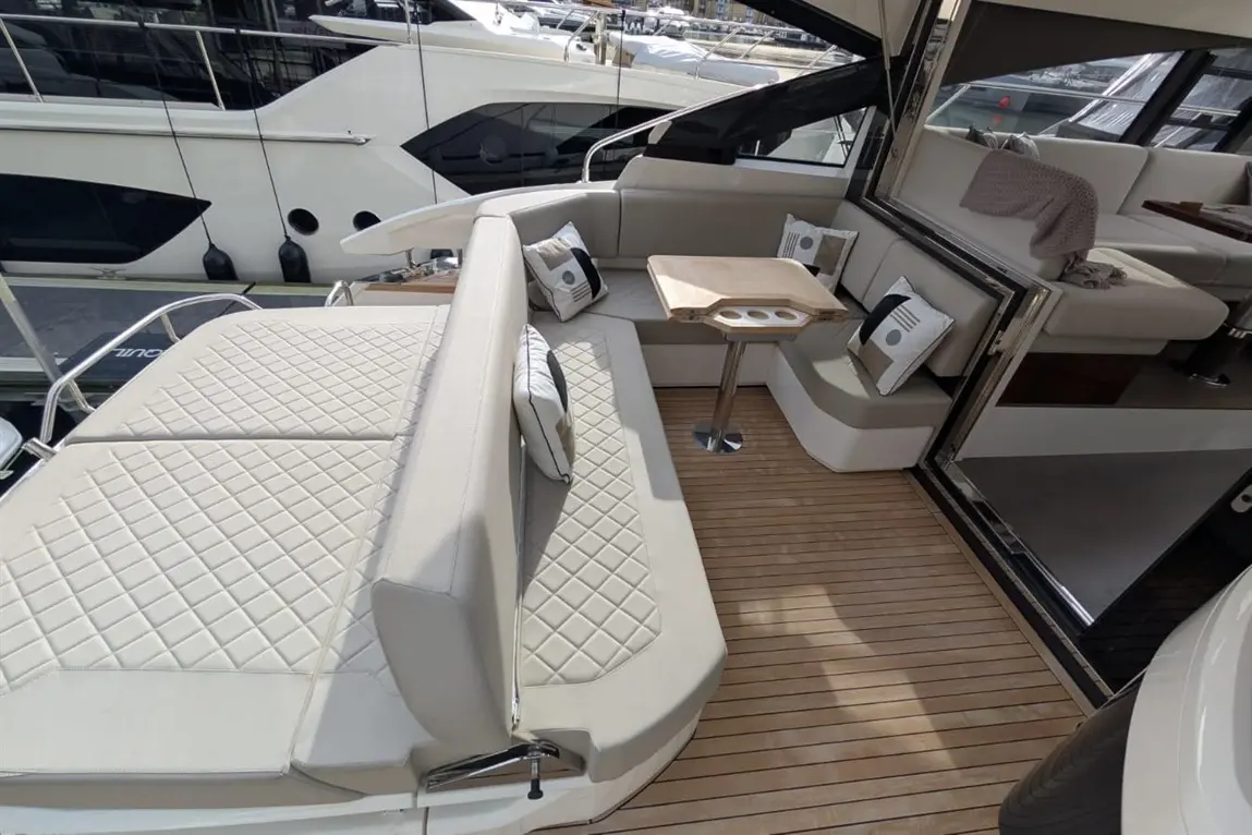 Luxurious yacht deck featuring modern seating, a wooden table, and decorative cushions against a backdrop of moored boats.