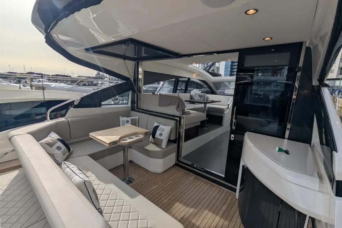 Luxurious yacht interior featuring a modern seating area, wooden deck, and views of the marina through large windows.