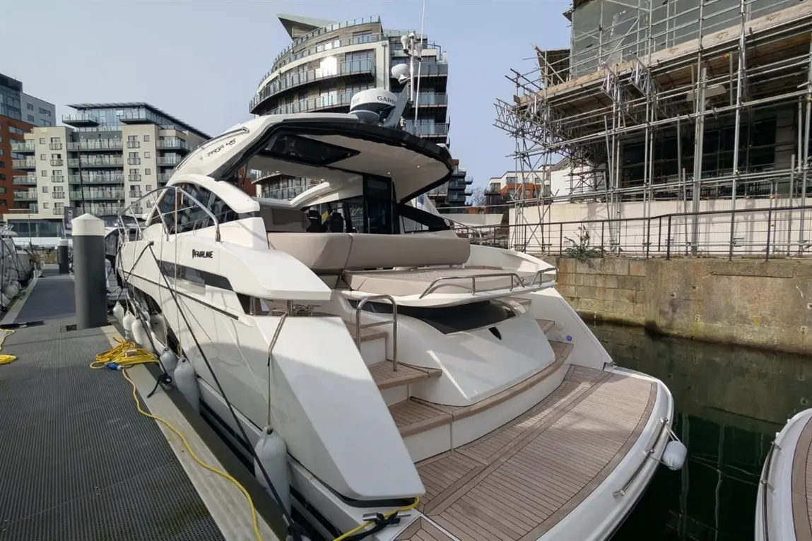 Luxury white motor yacht docked at a marina with modern apartments and scaffolding in the background.