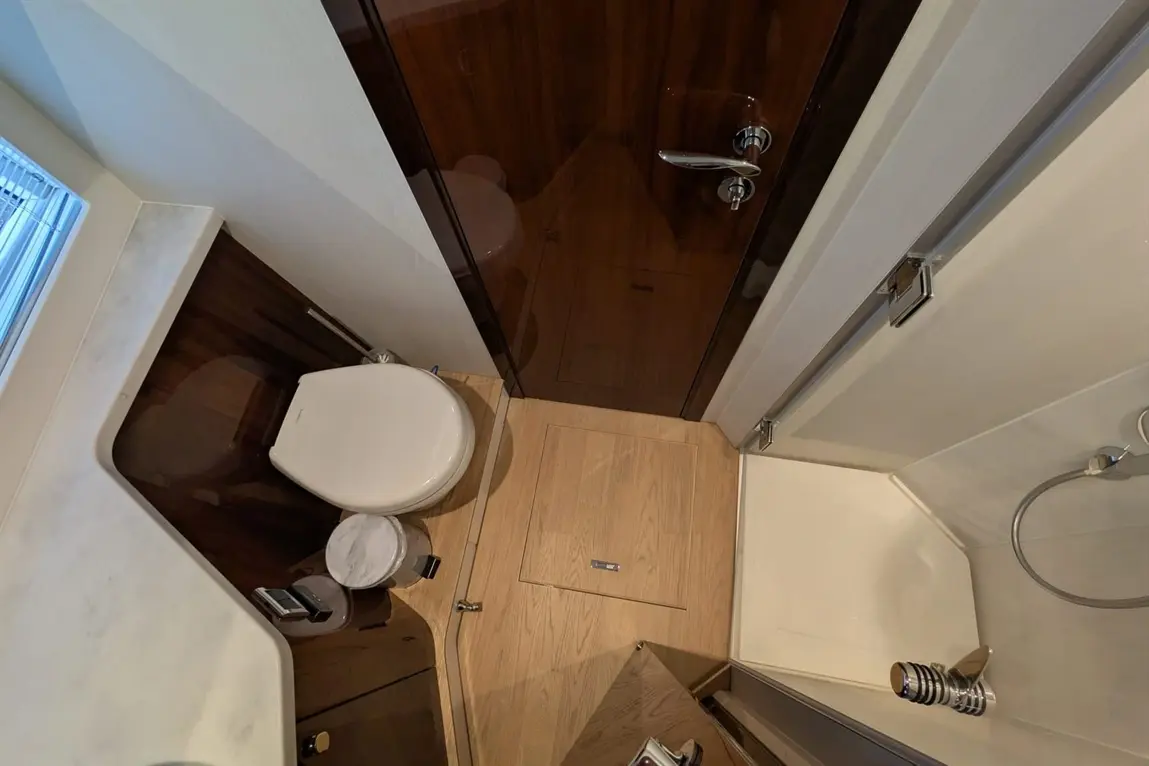 Compact modern bathroom featuring a toilet, shower, waste bin, and wooden flooring with a mirrored cabinet.
